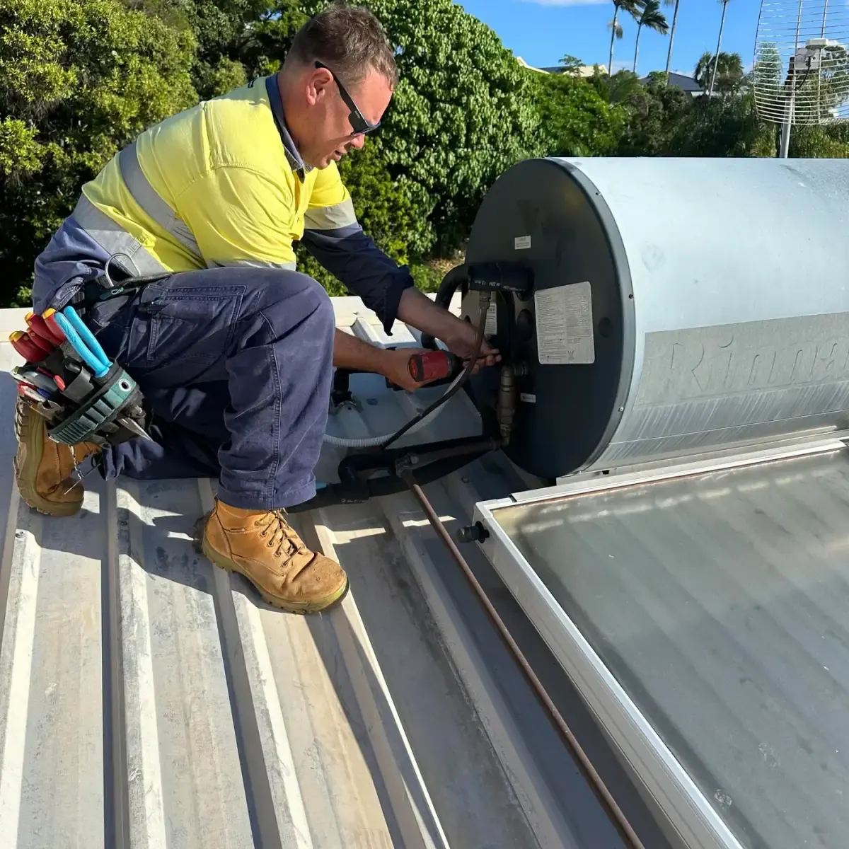 Kelly from Electrikell Qld in hi-vis working on a roof-mounted hot water unit in the Gladstone region