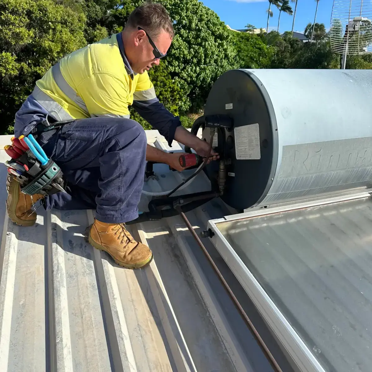 Kelly from Electrikell Qld in hi-vis working on a roof-mounted hot water unit in the Gladstone region